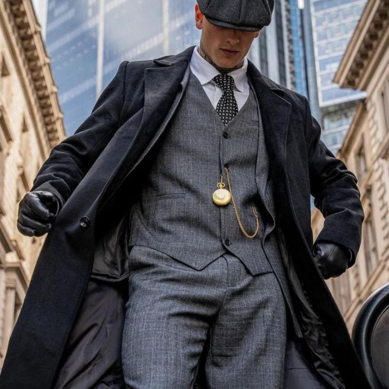 Man wearing a grey tweed three-piece suit with an overcoat and flat cap