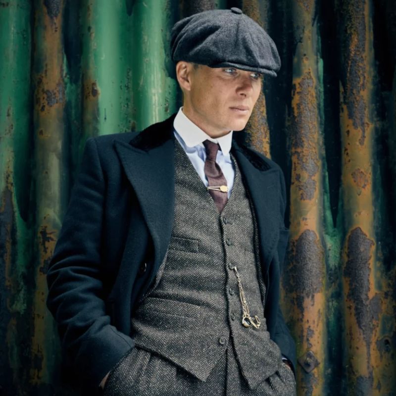 Man wearing a vintage grey herringbone suit with matching vest, overcoat and flat cap